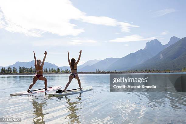 two stand up paddleboard ladies perform yoga moves - practioners enjoy serenity of paddleboard yoga stockfoto's en -beelden