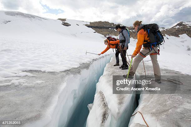 three mountaineers test crevasse edge on glacier - ice pick stock-fotos und bilder