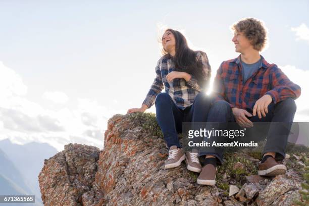 teen hikers relax on rock ridge above mtns - laughing teen stockfoto's en -beelden