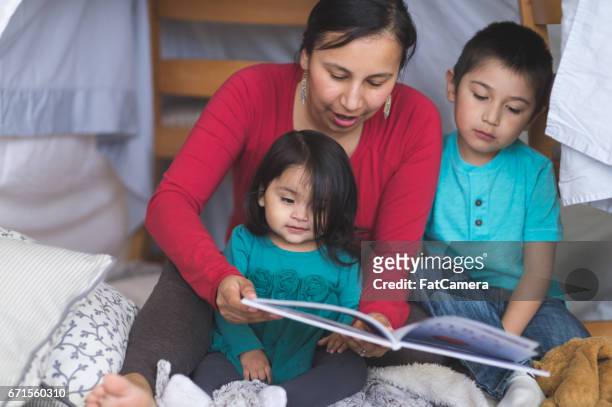 native american mom reads with her two children under makeshift fort in living room - indian fort stock pictures, royalty-free photos & images
