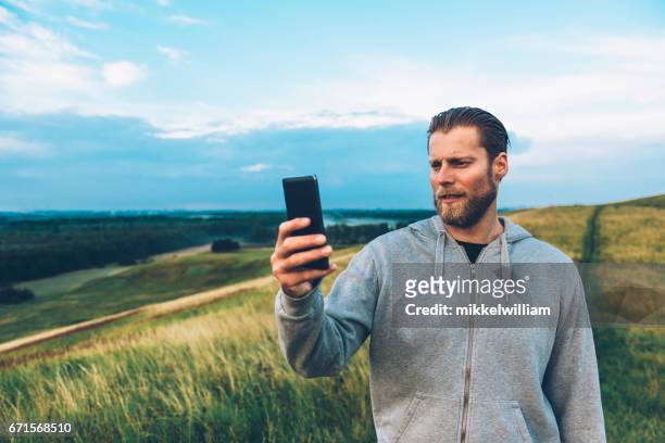man holds 4g smart phone while standing on a hill in a rural area - 4g stock pictures, royalty-free photos & images