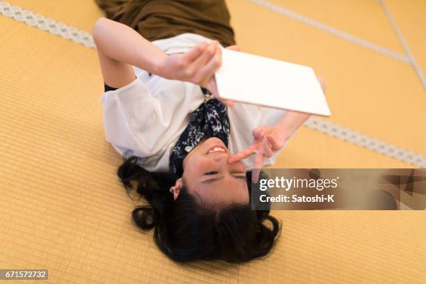 young woman lying on back and communicating with frineds through video chatting system on digital tablet - tatami mat stock pictures, royalty-free photos & images