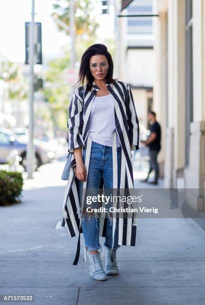 Olga wearing a striped coat, ripped denim jeans, glasses, boots on April 21, 2017 in Los Angeles, California.