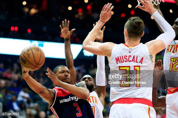 Bradley Beal of the Washington Wizards passes around Mike Muscala of the Atlanta Hawks under the basket during the fourth quarter in Game Three of...