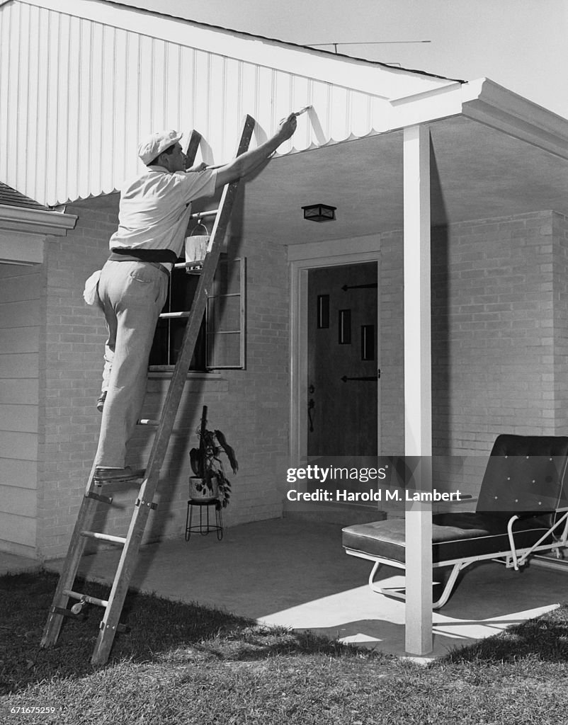   Man Standing On Ladder And Painting Roof 