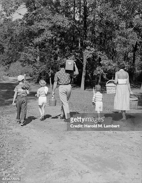 Family Walking With Picnic Paraphernalia In Park.