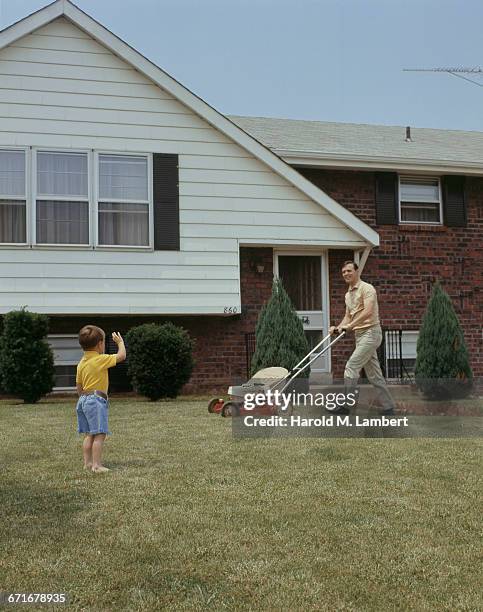 Father Looking At His Son While Mowing In Backyard .