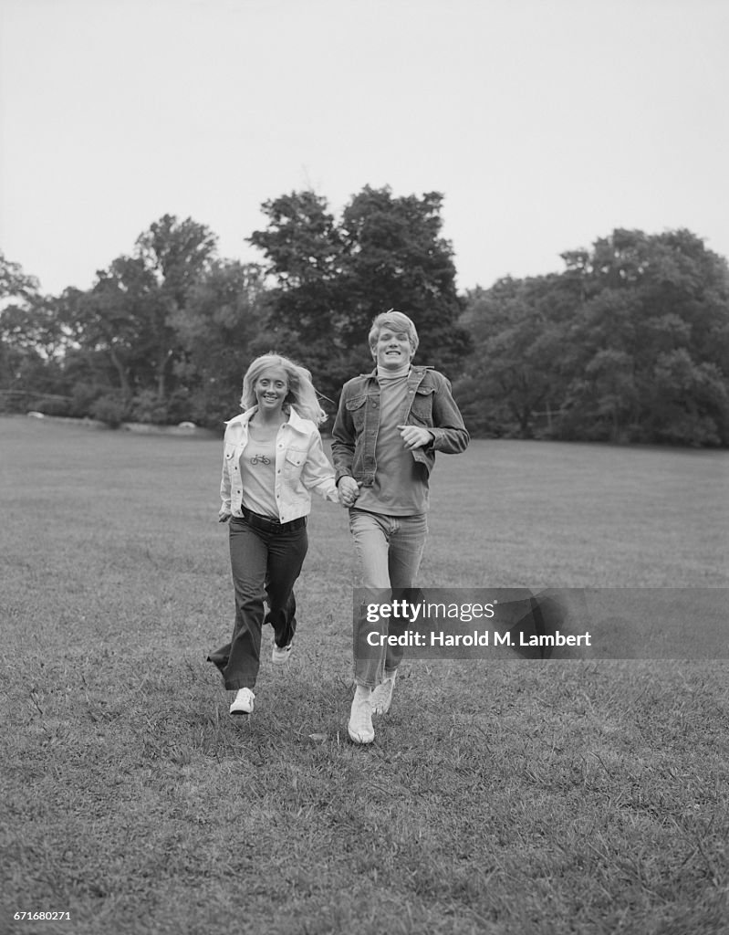  Teenage Couple Holding Hand And Running Through A Lawn