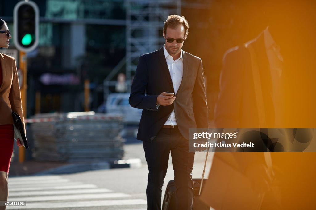 Businesspeople walking in pedestrian crossing with phones and bags