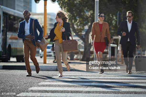 businesspeople running in pedestrian crossing with phones and bags - business women pants stock-fotos und bilder