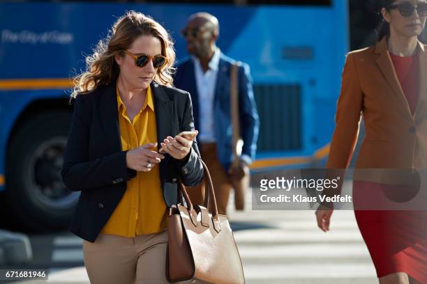 businesspeople walking in pedestrian crossing with phones and bags - schwarze handtasche stock-fotos und bilder