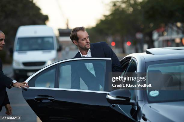 driver assisting businessman into cab - businessman taxi stock-fotos und bilder