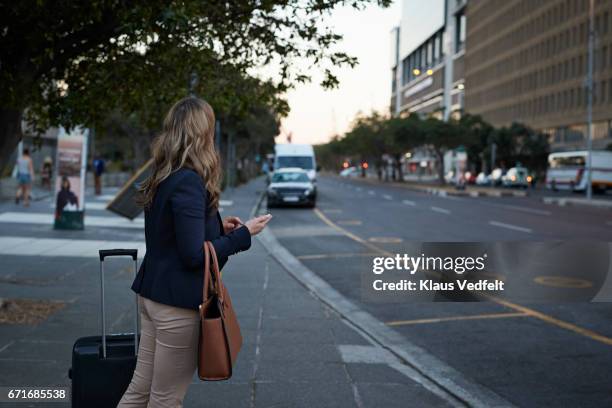 businesswoman with shoulder bag hailing a cab with her phone - calling a cab stock-fotos und bilder