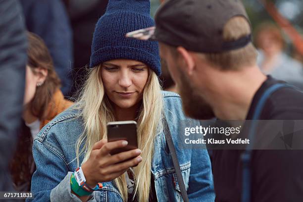 young woman checking phone at festival - coat music festival stock pictures, royalty-free photos & images