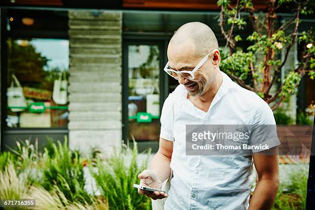 smiling man checking messages on smartphone - short sleeved 個照片及圖片檔