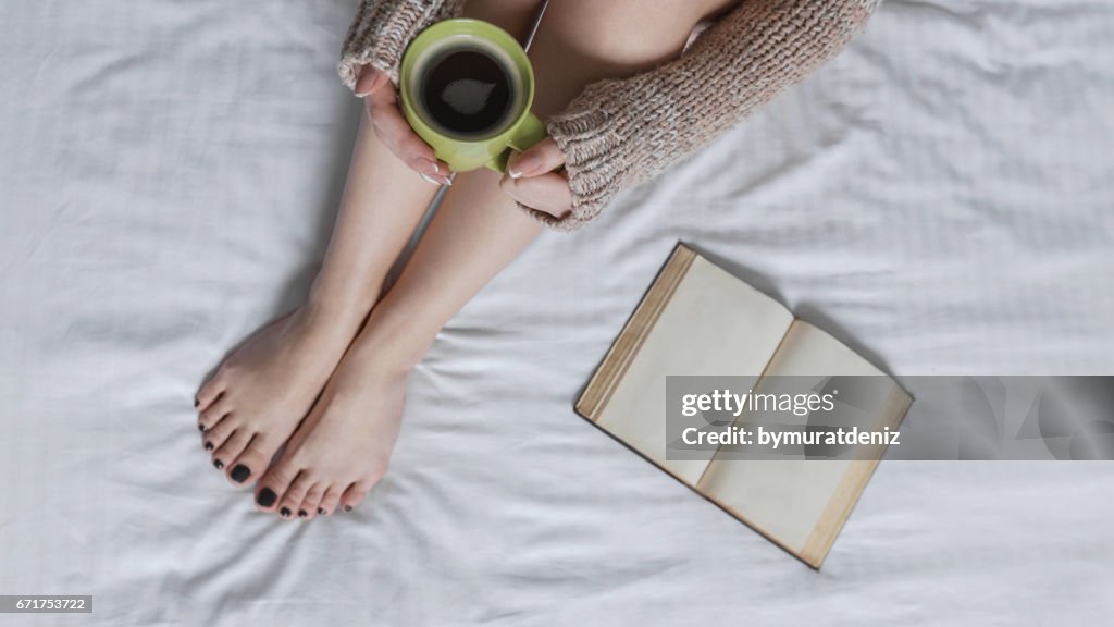 Jovem mulher lendo livro e bebendo café