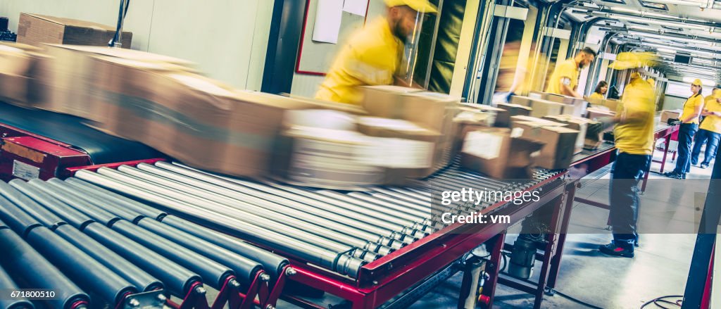 Trabalhadores dos correios inspecionando pacotes numa correia transportadora