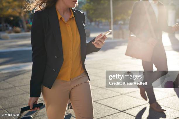 businesspeople walking across square looking at phones - luggage trolley stock-fotos und bilder