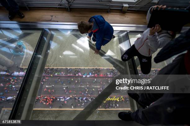 Spectators on the glass walkway of Tower Bridge take photographs of runners crossing the half way point on Tower Bridge during the London Marathon in...