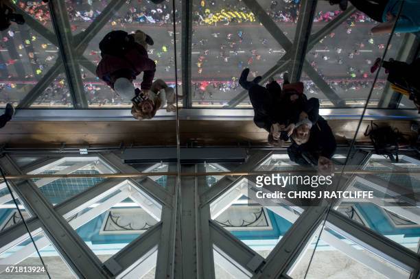 Spectators on the glass walkway of Tower Bridge take photographs of runners crossing the half way point on Tower Bridge during the London Marathon in...