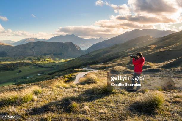 shot of a young man taking pictures from the coronet peak, queenstown, south island of new zealand. - extremlandschaft stock-fotos und bilder
