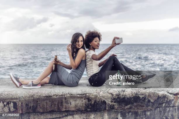 twee jonge cubaanse vrouw nemen selfie op de balustrade op de malecon in havanna - ballustrade stockfoto's en -beelden