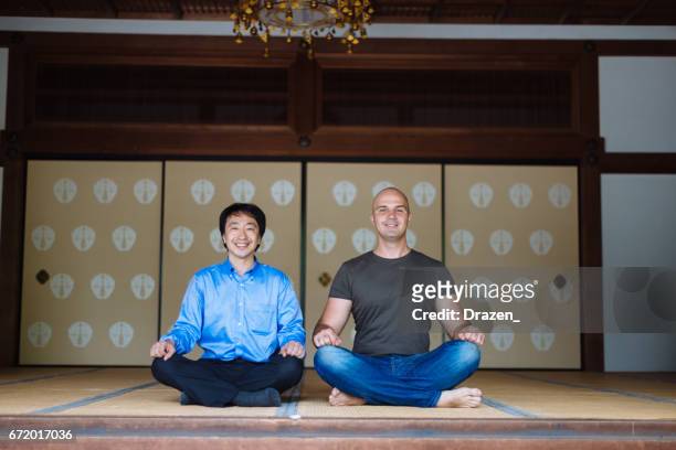 ヨーロッパの友人に神社で瞑想する方法を示す日本の男 - 胡坐　横 ストックフォトと画像