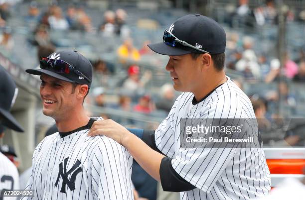 Masahiro Tanaka of the New York Yankees jokes with Greg Bird by massaging his shoulders in the dugout before the start of the first inning against...