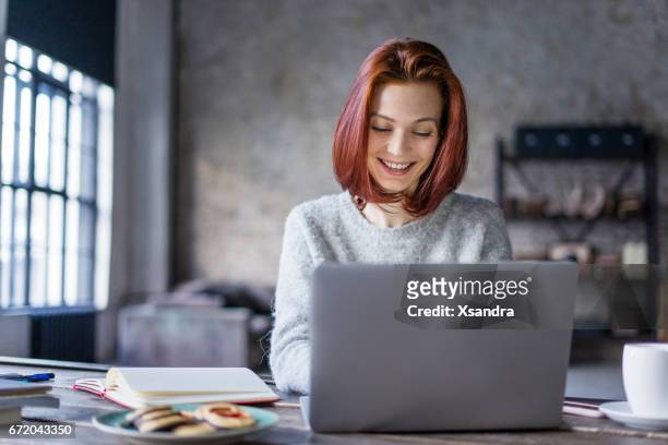jonge vrouw die werkt op een laptop in een loft - onafhankelijkheid stockfoto's en -beelden