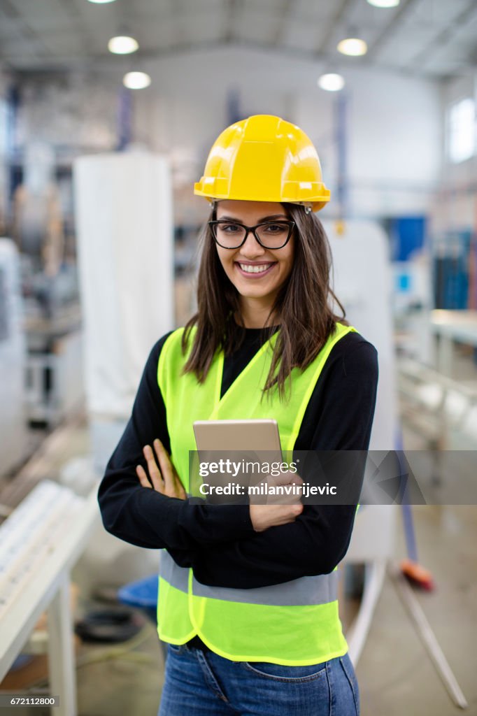 Beautiful girl at factory in a vest and helmet.
