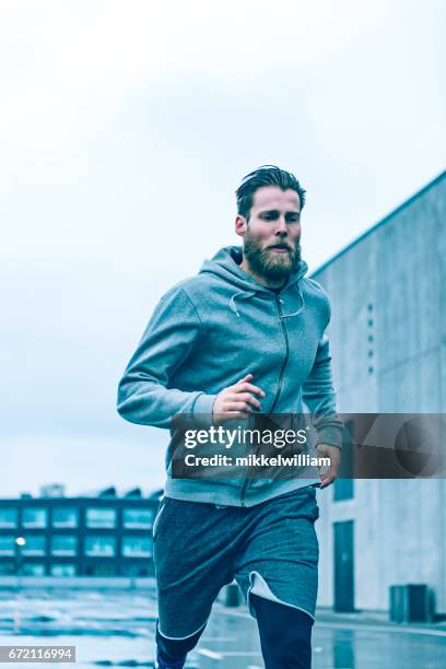 runner sprints fast as he runs outside on a grey day - guy beard city stock pictures, royalty-free photos & images