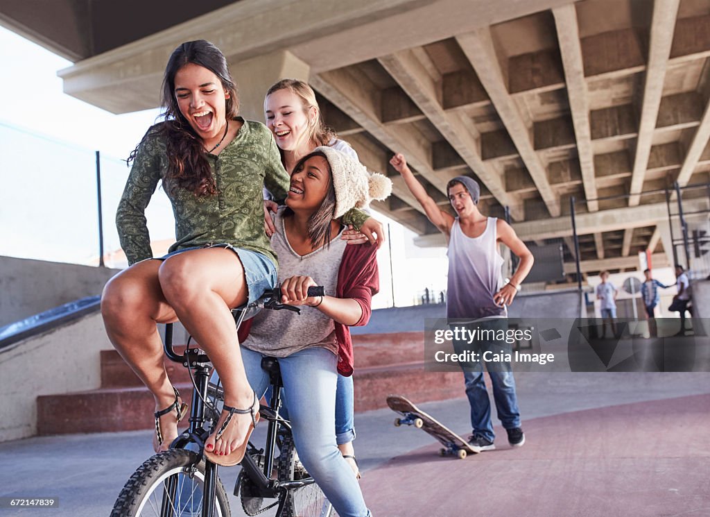 Playful teenage friends riding BMX bicycle and skateboarding at skate park