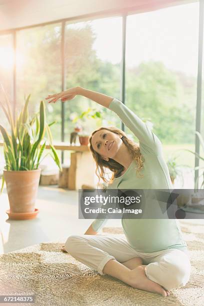 pregnant woman practicing yoga doing side stretch - schneidersitz stock-fotos und bilder