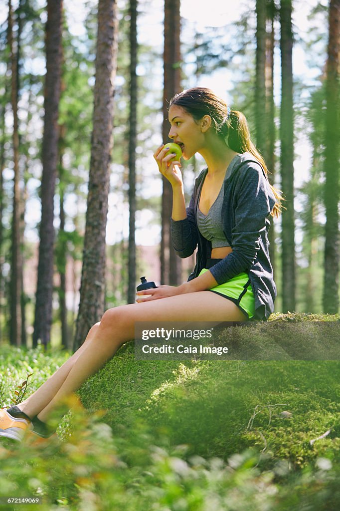 Runner resting eating apple on mossy rock in woods