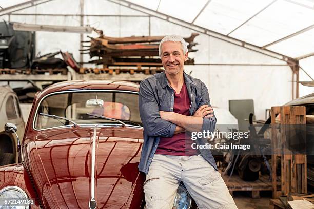 portrait confident mechanic leaning on classic car in auto repair shop - cofano foto e immagini stock