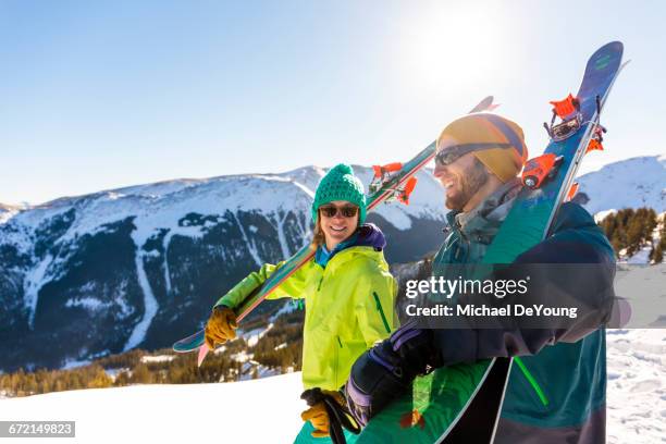 couple carrying skis on snowy mountain - vacaciones en la nieve fotografías e imágenes de stock