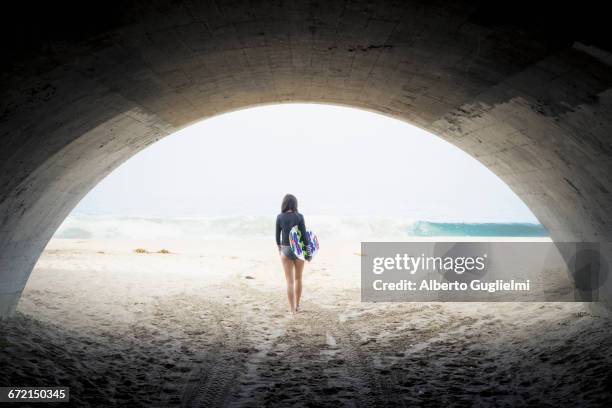 caucasian woman carrying skimboard under arch - leaving california stock pictures, royalty-free photos & images
