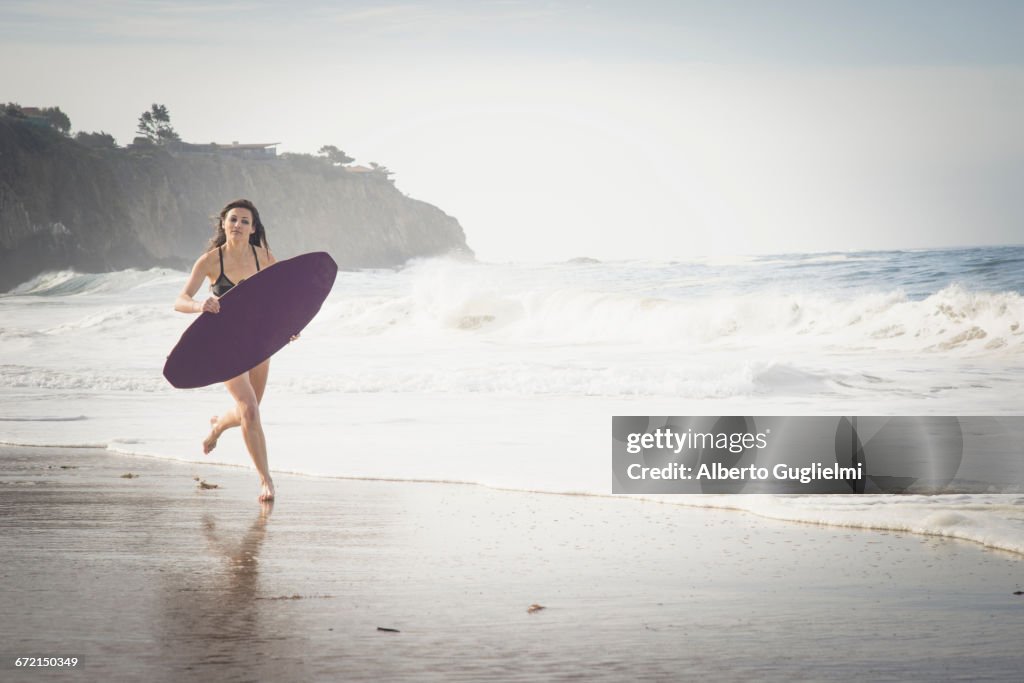 Caucasian woman running with skimboard at beach