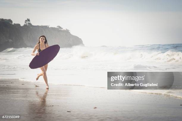 caucasian woman running with skimboard at beach - alberto guglielmi stock pictures, royalty-free photos & images