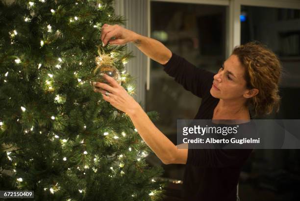 caucasian woman hanging ornament on christmas tree - alberto guglielmi imagens e fotografias de stock