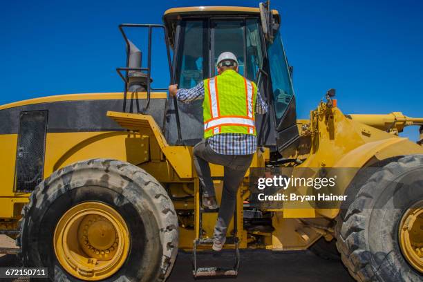 caucasian construction worker climbing onto earth mover - construction vehicle stock pictures, royalty-free photos & images
