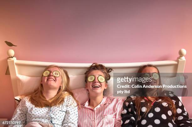 caucasian girls wearing cucumber slices on eyes in bed - slumber party - fotografias e filmes do acervo
