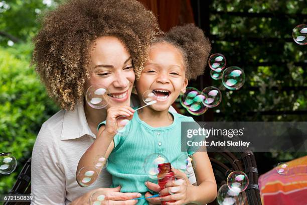 mixed race mother and daughter blowing bubbles - bubble wand photos et images de collection