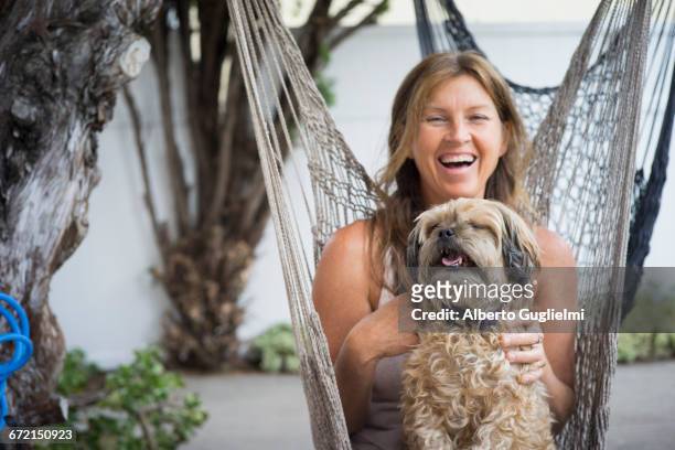 caucasian woman in hammock holding dog and laughing - alberto guglielmi imagens e fotografias de stock