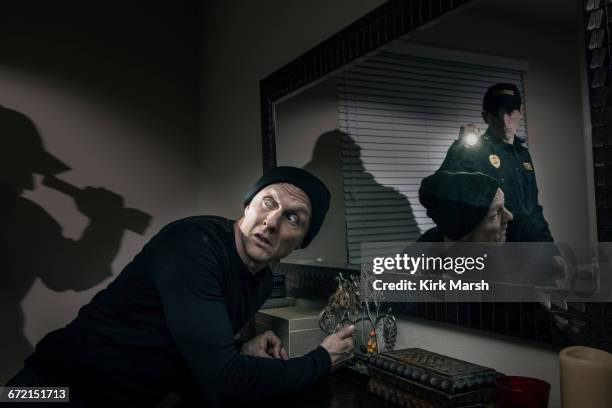 caucasian police officer shining flashlight on house burglar - burglary stock pictures, royalty-free photos & images