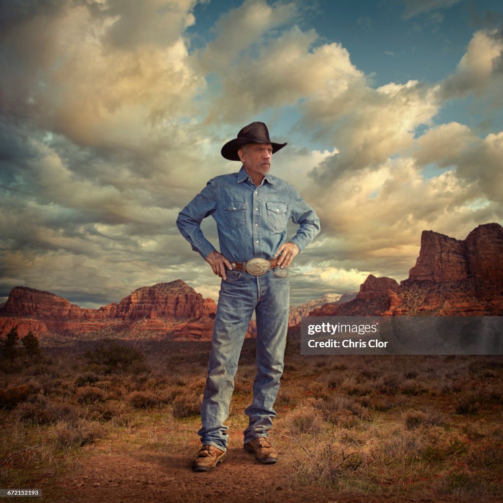 Caucasian cowboy standing with hands on hips in desert landscape