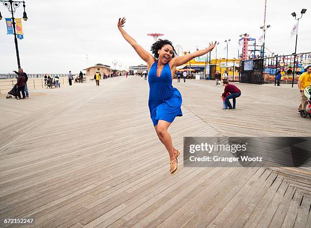 woman smiling and jumping on boardwalk at amusement park - parque de diversões edifício de entretenimento imagens e fotografias de stock