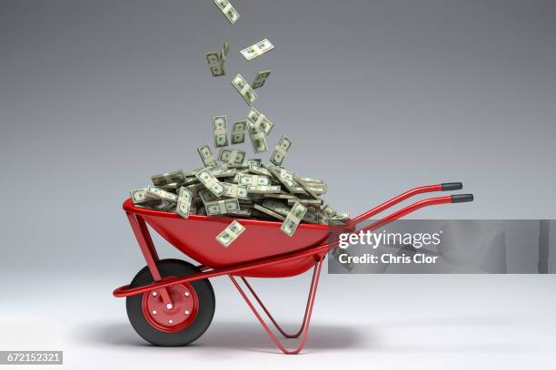 dollars falling into red wheelbarrow - money in wheelbarrow stockfoto's en -beelden
