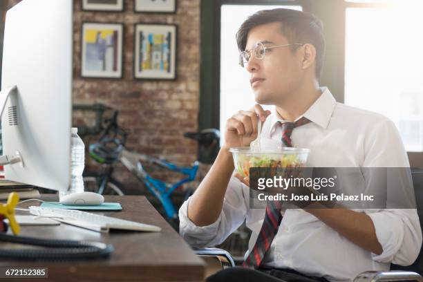 mixed race businessman using computer and eating salad at desk - シャツとネクタイ ストックフォトと画像