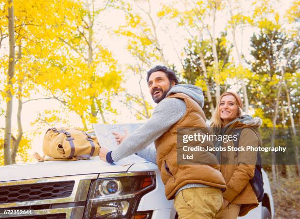 hispanic hikers leaning on car hood reading map - ski vest stock pictures, royalty-free photos & images